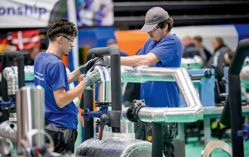 Teamarbeit an der Blechummantelung: Teilnehmende passen Blechsegmente an das gedämmte Rohrnetz an.