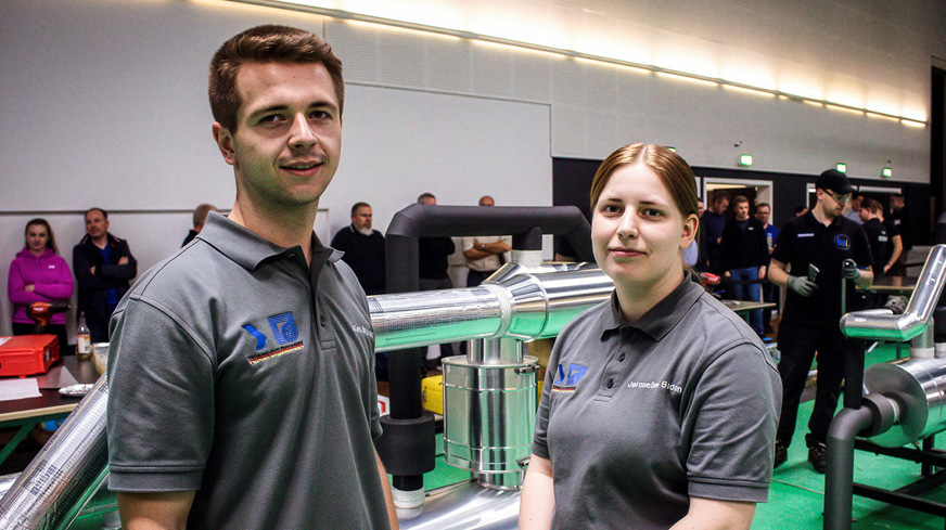 Deutsches Siegerteam im Fokus: Julian Brükner und Jacqueline Baden vor ihrem Wettbewerbsmodell – mit ihrer sauberen Dämmung, exakten Blechmontage und starkem Zeitmanagement gewinnen sie Gold.