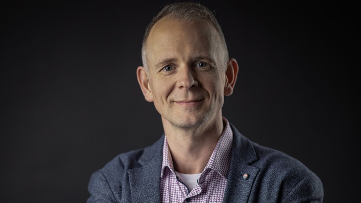 „Fachplaner in einem blauen Blazer und kariertem Hemd präsentiert innovative Dämmstofflösungen für verbesserte Energieeffizienz in der Gebäudetechnik.“. - © Thomas Schleicher