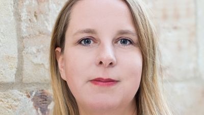 Eine Person mit langen blonden Haaren steht vor einer Steinmauer und blickt direkt in die Kamera. - © Elke Rieß 