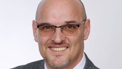 Ein lächelnder Mann mit Brille und Glatze, der ein graues Jackett und Hemd trägt. - © Jörg Meyer