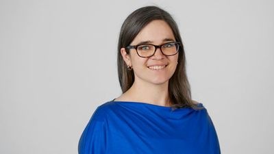 Person mit langen braunen Haaren, Brille und blauem Oberteil, lächelt vor einem schlichten Hintergrund. - © Karin Wiesemeyer