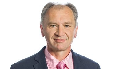 Ein Mann in Anzug und rosa Hemd mit Krawatte lächelt vor einem weißen Hintergrund. - © Karlheinz Kermann
