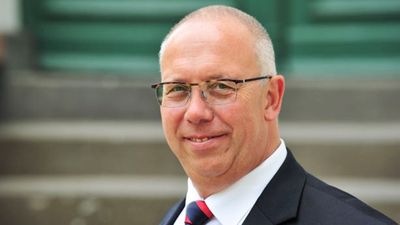 Lächelnder Mann im Anzug mit Brille, der im Freien vor verschwommenen Stufen und einer grünen Tür steht. - © Klaus-Peter Morgenstern