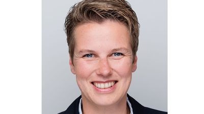 Lächelnde Person mit kurzen Haaren und dunklem Blazer vor hellgrauem Hintergrund. - © Vera Euhus