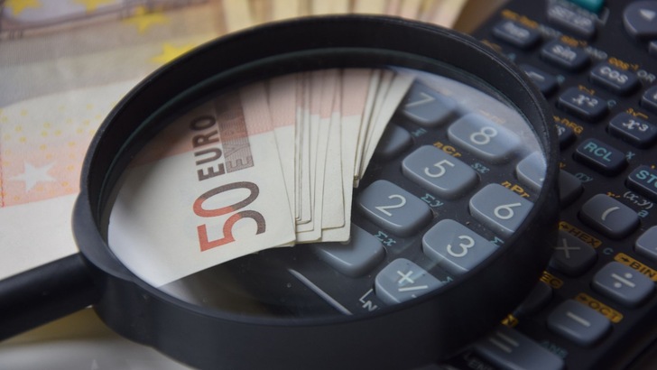 Eine Lupe liegt auf Geldscheinen und einem Taschenrechner