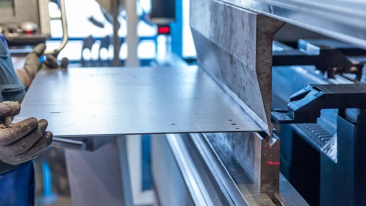 Person mit Sicherheitshandschuhen schiebt ein Metallblech in eine Maschine - © Michal Jarmoluk auf Pixabay