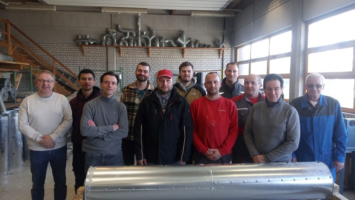 Die WKSB-Isolierer stehen in einer Schulungshalle. Im Hintergrund sind Modell-Isolier-Rohre zu sehen. Sie haben die Prüfungen bestanden und sind stolz. Alle lächeln in Richtung Kamera.