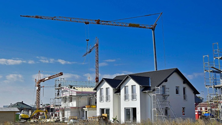 Das Bild zeigt im Bau befindliche Häuser in einem Neubaugebiet, Kräne und Baumaschinen