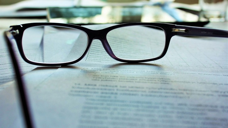 schwarz gerahmte Brille auf weißem Druckpapier - © Unsplash, Mari Helin