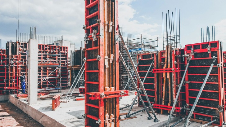 Das Bild zeigt eine aktive Baustelle mit mehreren Schalungselementen und Stahlbewehrungen, die für die Errichtung einer Betonstruktur vorbereitet werden. - © Unsplash, Di
