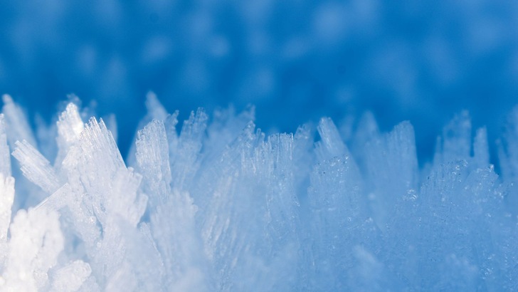 Detaillierte Nahaufnahme von eisigen Frostkristallen, die bei Kälte entstanden sind und ein natürliches Muster bilden.