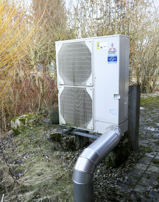 Außenklimaanlage mit zwei Ventilatoren, installiert auf einer Steinplatte, umgeben von trockenen Pflanzen und Pflaster. - © Foto: Karlheinz Kermann