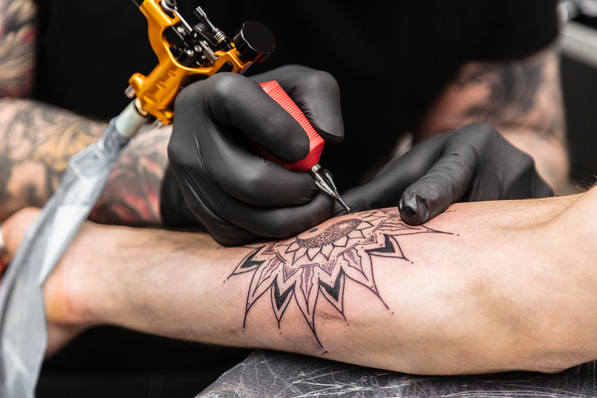 Process of creating tattoo in form of black flower. Master does work in sterile gloves